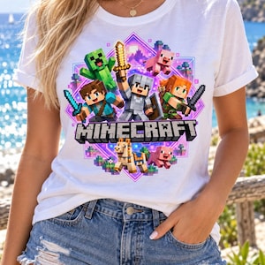 Puede incluir: Una camiseta blanca con un estampado gráfico colorido de personajes de Minecraft, incluyendo un Creeper, Steve, Alex, un cerdo y un caballo, centrados en un marco de diamante morado con la palabra MINECRAFT impresa en letras negras negritas.