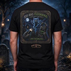 May include: A black t-shirt featuring a graphic on the back with the text BOO-WHO PARANORMAL RESEARCH SOCIETY EVP TECHNICIAN and BUNK INDUSTRIES. The design shows a ghostly cat, a flashlight, and a digital recorder in a graveyard setting.