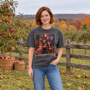 May include: A charcoal gray short-sleeve t-shirt featuring a rectangular graphic print of anthropomorphic cats dressed in Halloween costumes, including witch and vampire attire, holding jack-o'-lanterns, with the text "Halloween by Cheryl".