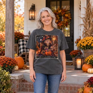 May include: A charcoal grey short-sleeve t-shirt featuring a graphic print of a cat wearing a witch hat and holding a broomstick, with a pumpkin bucket filled with candy. The text reads "Meow by Chief" and "Ghouls Goes Halloween '88".