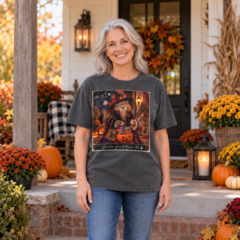 May include: A charcoal grey short-sleeve t-shirt featuring a graphic print of a cat wearing a witch hat and holding a broomstick, with a pumpkin bucket filled with candy. The text reads "Meow by Chief" and "Ghouls Goes Halloween '88".