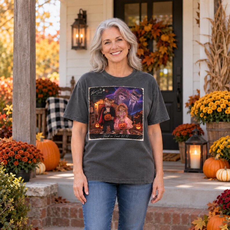 May include: A charcoal grey short-sleeve t-shirt featuring a graphic print of three cats dressed in Halloween costumes, including a vampire and a princess, with the text Trick or Treat 87.19 and a dark, atmospheric, spooky autumn background.