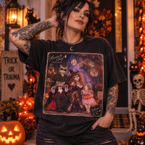 Pu&ograve; includere: Una t-shirt nera lavata all'acido con una stampa grafica di una famiglia di gatti in costume di Halloween. Il testo recita Memories by Cheryl, Portrait Studio, Living, Loving, Make Beautiful Memories, Trick or Trauma e Halloween 87.