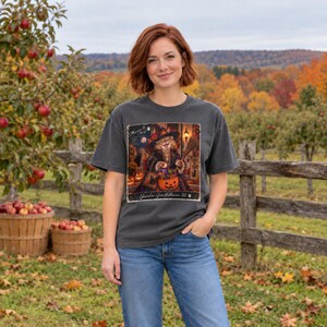 May include: A charcoal gray short-sleeve t-shirt featuring a graphic print of a cat dressed as a witch holding a broom and a pumpkin bucket filled with candy. The text on the graphic reads 'Halloween is Coming' and 'Grandma Gets Halloween'.