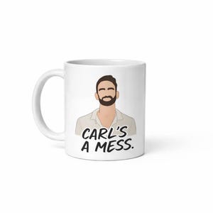 May include: White ceramic mug featuring a cartoon illustration of a man with a beard and the text "CARL'S A MESS." The mug has a curved handle and a glossy finish. The illustration is in shades of brown, black, and white.