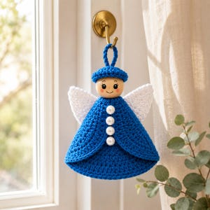May include: A crocheted angel ornament featuring a blue dress, a matching blue hat, and white wings. The figure has a round wooden head with a painted face and four white pearl-like beads arranged vertically down the center of the blue dress.