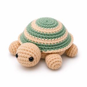 May include: A crochet turtle toy featuring a rounded shell with alternating concentric rings of sage green and cream yarn. The head, four legs, and underside are crafted from solid cream yarn, and the turtle has two small, round, black plastic eyes.