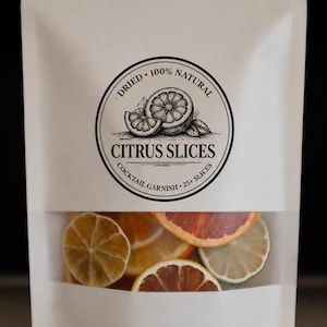 Könnte beinhalten: Ein weißer Beutel mit einem transparenten Fenster, das getrocknete Zitrusfruchtscheiben zeigt. Der Beutel hat ein rundes Etikett mit dem Text "Dried 100% Natural Citrus Slices Cocktail Garnish 25+ Slices" und eine Zitrusfruchtgrafik.