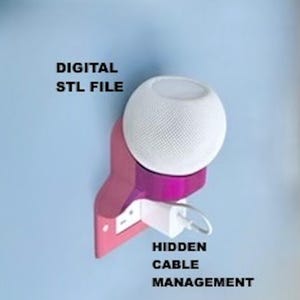 May include: A pink wall-mounted speaker holder with a white spherical speaker resting on top. The mount features a white power adapter plugged into a wall outlet with a white cable. Text reads: DIGITAL STL FILE and HIDDEN CABLE MANAGEMENT.