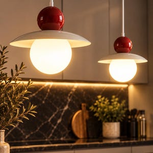 Peut inclure: Deux suspensions lumineuses composées d'une sphère supérieure rouge brillante, d'un abat-jour blanc en forme de disque et d'une ampoule en verre sphérique blanche diffusant une lumière chaude. Elles sont suspendues par de fines tiges blanches.