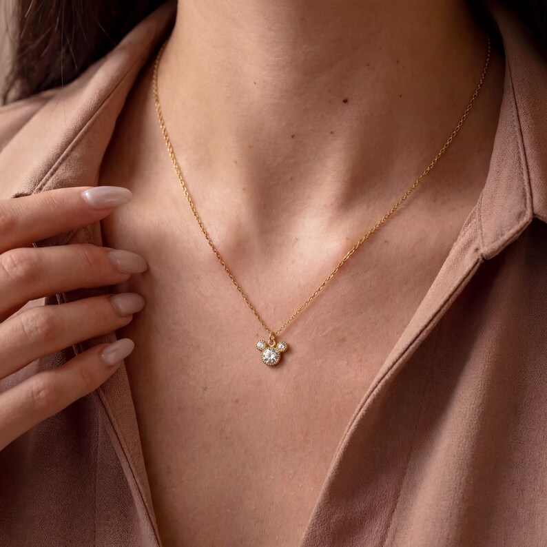 May include: A gold necklace with a pendant featuring three clear stones. The central stone is larger than the two flanking it. The necklace is suspended against a neutral background, highlighting the pendant's design.