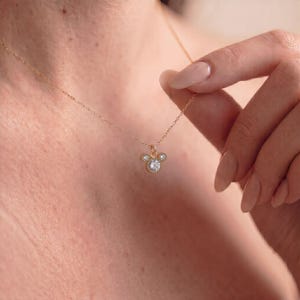 Puede incluir: Un collar de cadena dorada fina con un colgante en forma de silueta de cabeza de ratón. El colgante está elaborado con tres piedras claras de corte redondo, con una piedra central más grande y dos piedras más pequeñas a los lados, engastadas en oro.