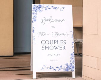Può includere: Un cartello bianco a forma di A con decorazioni floreali blu e la scritta "Welcome to Tatum & Greer's Couples Shower 07-12-27 Dallas, TX". Adatto per un matrimonio o un baby shower.