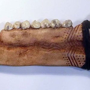 May include: A brown bone-like knife with a black leather wrap and white teeth-like protrusions.