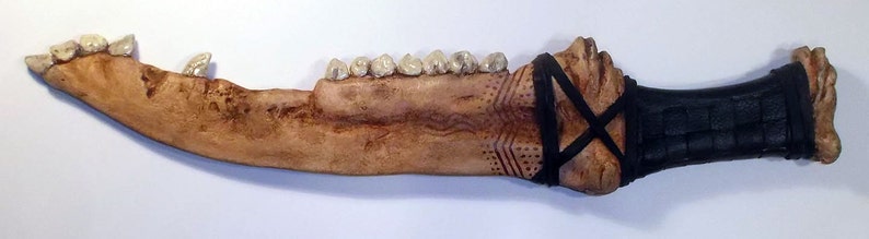 May include: A brown bone-like knife with a black leather wrap and white teeth-like protrusions.