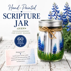 Puede incluir: Un frasco de vidrio transparente con tapa de metal plateado y un lazo de cuerda de yute. El frasco tiene flores de lupino azules y hierba verde pintadas a mano. Contiene tiras de papel blanco. Texto: Hand-Painted SCRIPTURE JAR, 60 BIBLE VERSES.