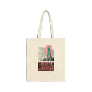 May include: Cream-colored tote bag with a graphic design. The design features a person with a pineapple head, set against a backdrop of a cloudy sky and a red-orange square. The bottom portion shows legs. The bag has two handles.