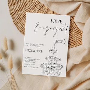 Könnte beinhalten: Verlobungsankündigungskarte in Schwarzweiß mit der Aufschrift "WE'RE Engaged!". Das Design zeigt eine Champagnerflasche, die in einen Turm aus Gläsern gießt. Details: Namen, Datum, Uhrzeit und RSVP-Informationen.