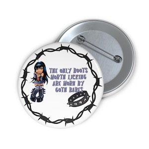 Może przedstawiać: Dwa białe, okrągłe guziki. Jeden guzik przedstawia kreskówkową gotycką dziewczynę, obrożę z ćwiekami i fioletowy napis "THE ONLY BOOTS WORTH LICKING ARE WORN BY GOTH BABES". Drugi guzik jest częściowo widoczny.