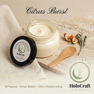 May include: A jar of Citrus Burst body butter with a black lid, a wooden spoon, and dried orange peel. The jar is open, revealing the creamy body butter. The text "Citrus Burst" is at the top of the image. The product is 6 oz.