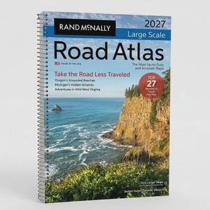 May include: A 2027 Rand McNally Large Scale Road Atlas with a spiral binding. The cover features a coastal landscape with a rocky cliff and ocean. Text includes 'Take the Road Less Travelled', 'Top 27 Reasons to Travel This Year', and '35% Larger Maps'.