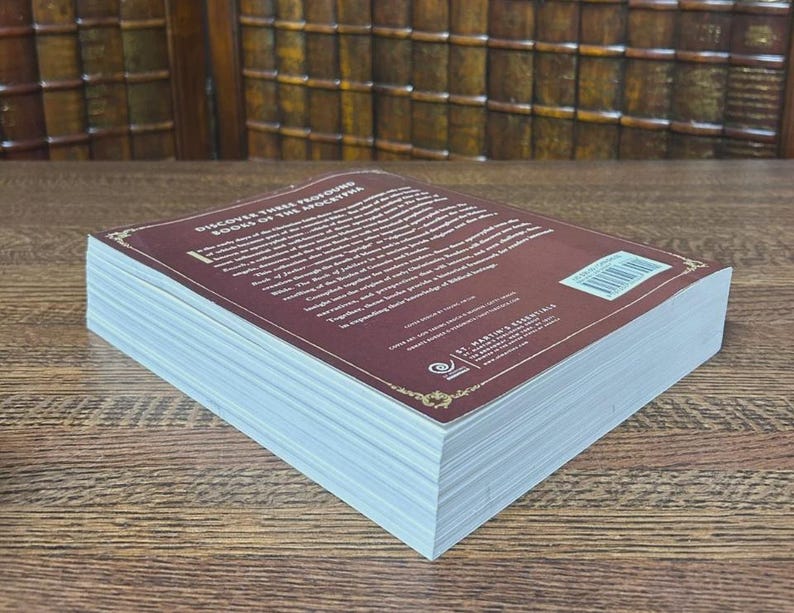 K&ouml;nnte beinhalten: Ein Hardcover-Buch mit einem weinroten Einband und wei&szlig;en Seiten. Der Einband tr&auml;gt den wei&szlig;en Text "Discover These Profound Books of the Apocrypha". Das Buch liegt auf einer Holzoberfl&auml;che.