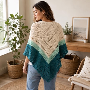 Op de afbeelding: Een gehaakte poncho met een V-vormig ontwerp en een kleurverloop van crème aan de bovenkant naar licht muntgroen in het midden en diepblauwgroen aan de onderrand, afgewerkt met een ingewikkelde, kantachtige geschulpte rand.
