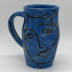 May include: A white ceramic mug with a black handle and the text "But First, Coffee" in a handwritten style. The mug is on a white surface. The mug is 4 inches tall.