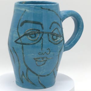 May include: A white ceramic mug with a black handle and the text "But First, Coffee" in a handwritten style. The mug is on a white surface. The mug is 4 inches tall.