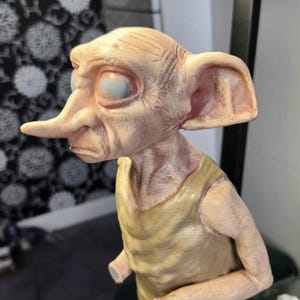 Op de afbeelding: Gedetailleerd beeldje van een personage met grote oren, een lange neus en een bleke huid. Het beeldje draagt een bruine tuniek. De ogen zijn lichtblauw. Het beeldje is een representatie van een fantasiepersonage.