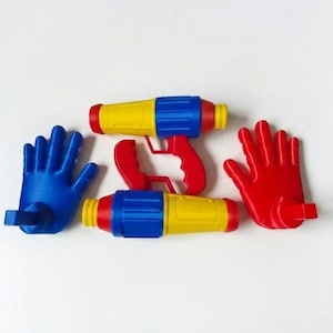 May include: Two yellow, blue, and red water guns with a red handle and two hand-shaped toys, one blue and one red. The toys are arranged on a white background. The water guns have a cylindrical shape.