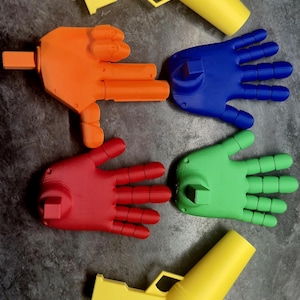 May include: An assortment of colorful, 3D-printed hand-shaped objects and toy guns in yellow, orange, red, blue, and green. The hands are open, with fingers extended. The toy guns are cylindrical with a trigger.