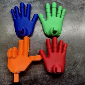 May include: Four colorful, 3D-printed hands in blue, green, orange, and red. The hands are arranged in a square, with each hand facing a different direction. The hands appear to be made of plastic and have a smooth finish.