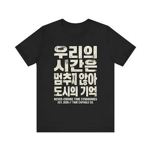 Puede incluir: Camiseta negra con texto coreano en una fuente blanquecina desgastada. El texto incluye frases como "Nuestro tiempo" y "Memoria de la ciudad". Debajo del texto coreano está el texto en inglés "NEVER-ENDING TIME SYNDROMES EST. 2026 // TIME CAPSULE CO."