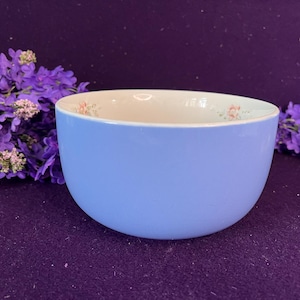May include: A smooth, light blue ceramic bowl with a rounded shape. The interior of the bowl features a white surface decorated with small, delicate floral patterns in soft pink and green hues along the upper inner rim of the vessel.
