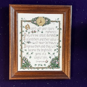 May include: A framed cross-stitch sampler featuring the text: Guard well your spare moments. They are like uncut diamonds. Discard them and their value will never be known. Improve them and they will become the brightest gems in a useful life. Emerson.