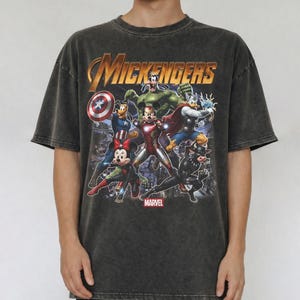 May include: A charcoal grey acid-wash t-shirt featuring a graphic print titled MICKENGERS with Disney characters dressed as Marvel superheroes, including Mickey Mouse as Iron Man, Minnie Mouse as Black Widow, and Goofy as the Hulk.