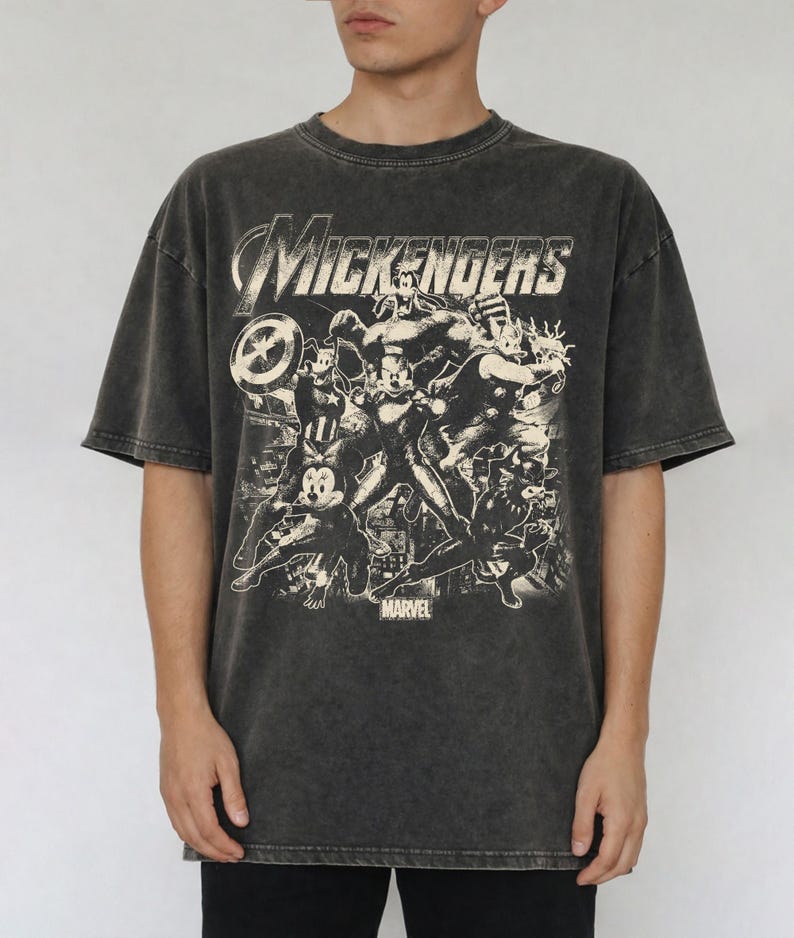 以下が含まれることがあります： チャコールグレーの酸洗い加工が施された半袖Tシャツ。スーパーヒーローの格好をした漫画キャラクターのグラフィックプリントが特徴です。上部には「MICKENGERS」の文字があり、グラフィックの下部には小さなフォントで「MARVEL」という言葉がプリントされています。