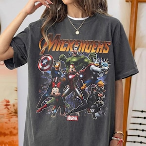 May include: A charcoal gray crewneck t-shirt featuring a graphic print titled MICKENGERS with cartoon characters dressed as superheroes. The design includes characters resembling Mickey, Minnie, Goofy, and Donald Duck in various hero costumes, with the Marvel logo below.