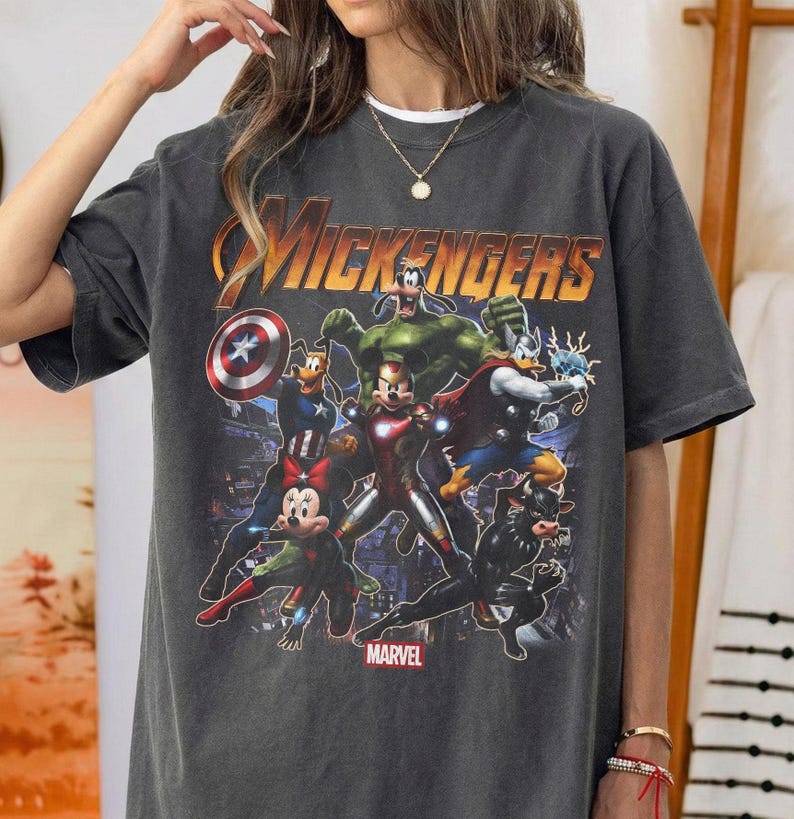 May include: A charcoal gray crewneck t-shirt featuring a graphic print titled MICKENGERS with cartoon characters dressed as superheroes. The design includes characters resembling Mickey, Minnie, Goofy, and Donald Duck in various hero costumes, with the Marvel logo below.