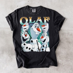 May include: A black short-sleeve t-shirt featuring a graphic print of five Olaf characters from Frozen. The word OLAF is printed in large, stylized letters above the characters, which are set against a blue and green background with lightning.