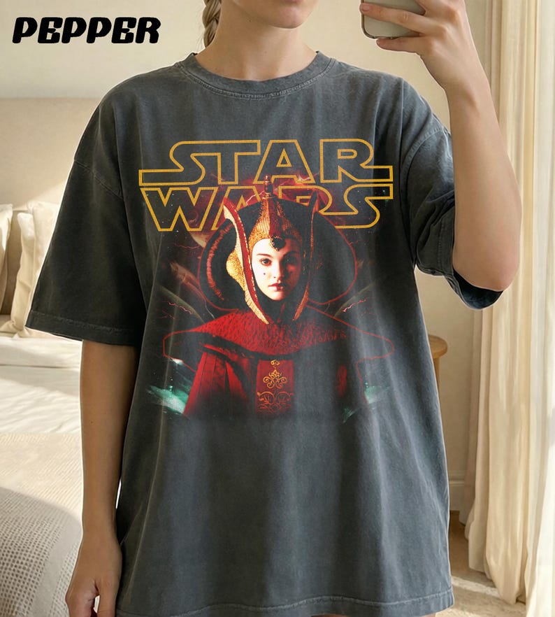 Puede incluir: Camiseta gris oscuro con un gr&aacute;fico de Star Wars. El texto amarillo dice "STAR WARS", y la imagen muestra un personaje con atuendo rojo y dorado. La palabra "PEPPER" est&aacute; impresa en la esquina superior izquierda.