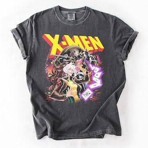 May include: Dark gray t-shirt featuring a colorful graphic of X-Men characters Rogue and Gambit. The X-MEN logo is in yellow and red. The shirt is made of a soft material and has a vintage wash.
