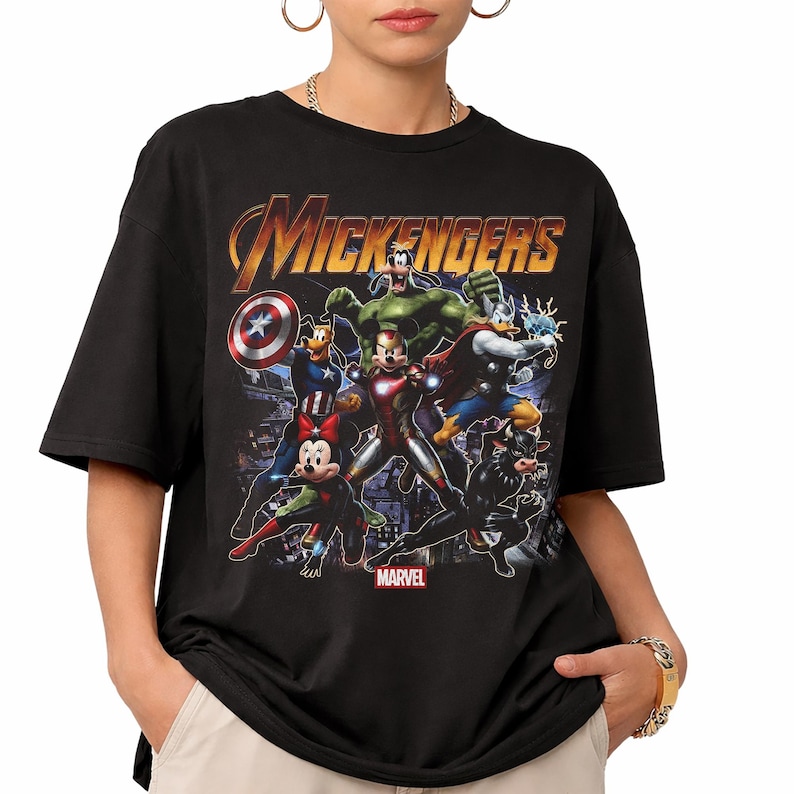 May include: A black short-sleeve t-shirt featuring a graphic print titled MICKENGERS. The design displays cartoon characters dressed as superheroes, including Mickey Mouse as Iron Man, Minnie Mouse as Black Widow, and Goofy as Hulk.