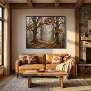 Puede incluir: Un cuadro rectangular enmarcado que representa una escena forestal con &aacute;rboles grandes, follaje oto&ntilde;al en tonos naranja y marr&oacute;n, y un sendero que se pierde en la distancia, exhibido en un marco negro sobre un sof&aacute; de cuero color canela.