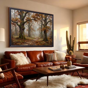 Puede incluir: Una gran obra de arte mural rectangular enmarcada que representa una escena de bosque brumoso con &aacute;rboles altos y follaje oto&ntilde;al en tonos marrones, naranjas y verdes, montada sobre un sof&aacute; de cuero marr&oacute;n con cojines texturizados.