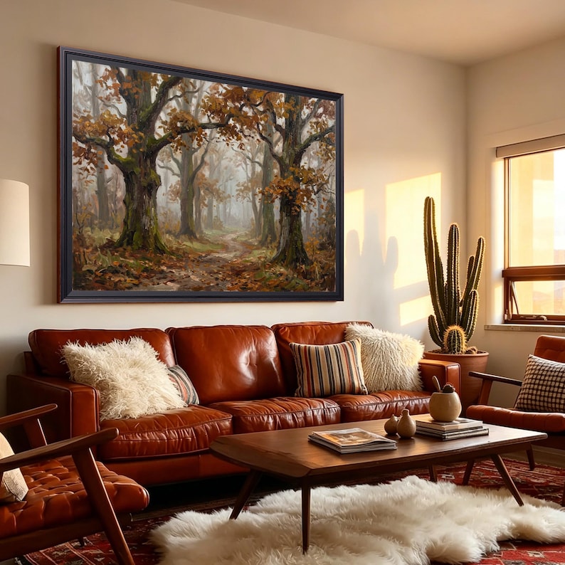 Puede incluir: Una gran obra de arte mural rectangular enmarcada que representa una escena de bosque brumoso con &aacute;rboles altos y follaje oto&ntilde;al en tonos marrones, naranjas y verdes, montada sobre un sof&aacute; de cuero marr&oacute;n con cojines texturizados.