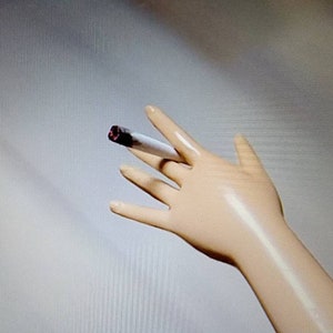 May include: A close-up of a white mannequin hand holding a lit cigarette.