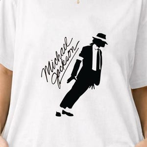 Könnte beinhalten: Weißes T-Shirt mit einer schwarzen Silhouette von Michael Jackson in einer charakteristischen Pose und dem Namen "Michael Jackson" in Schreibschrift. Das Shirt hat einen klassischen Rundhalsausschnitt.