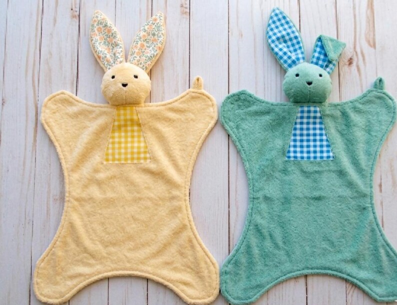 May include: Two plush bunny security blankets. One is yellow with floral print ears and a yellow gingham patch. The other is teal with blue gingham ears and a blue gingham patch. Both have a bunny head and a soft, textured body.